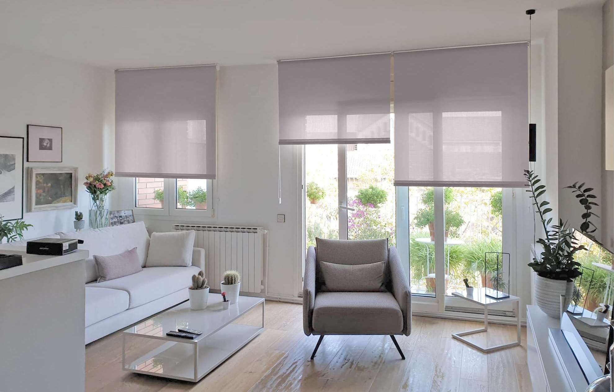 Salón luminoso con estores enrollables claros a media altura en las ventanas