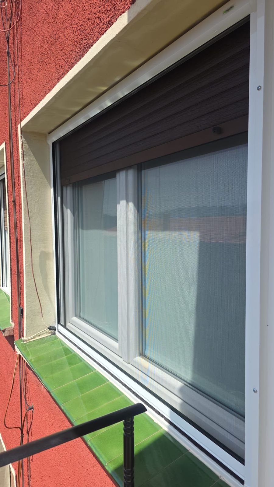 Ventana blanca con persiana marrón y mosquitera enrollable bajada