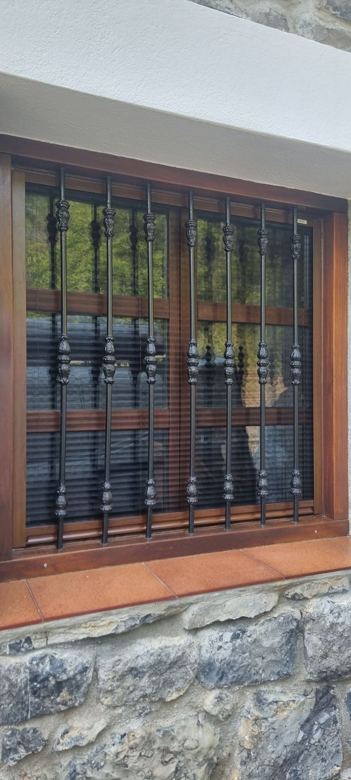 Ventana de madera con reja de forja y mosquitera plisada imitación madera