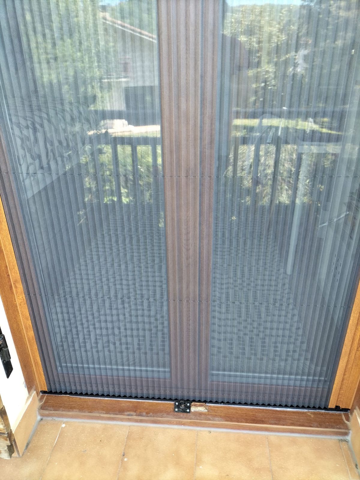 Puerta de terraza de dos hojas con mosquitera plisada cerrada y marco color madera